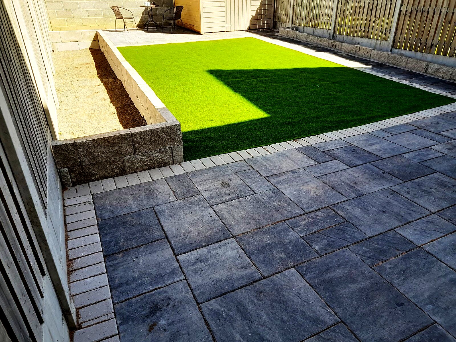 Grey paved patio with raised planter and bright artificial grass